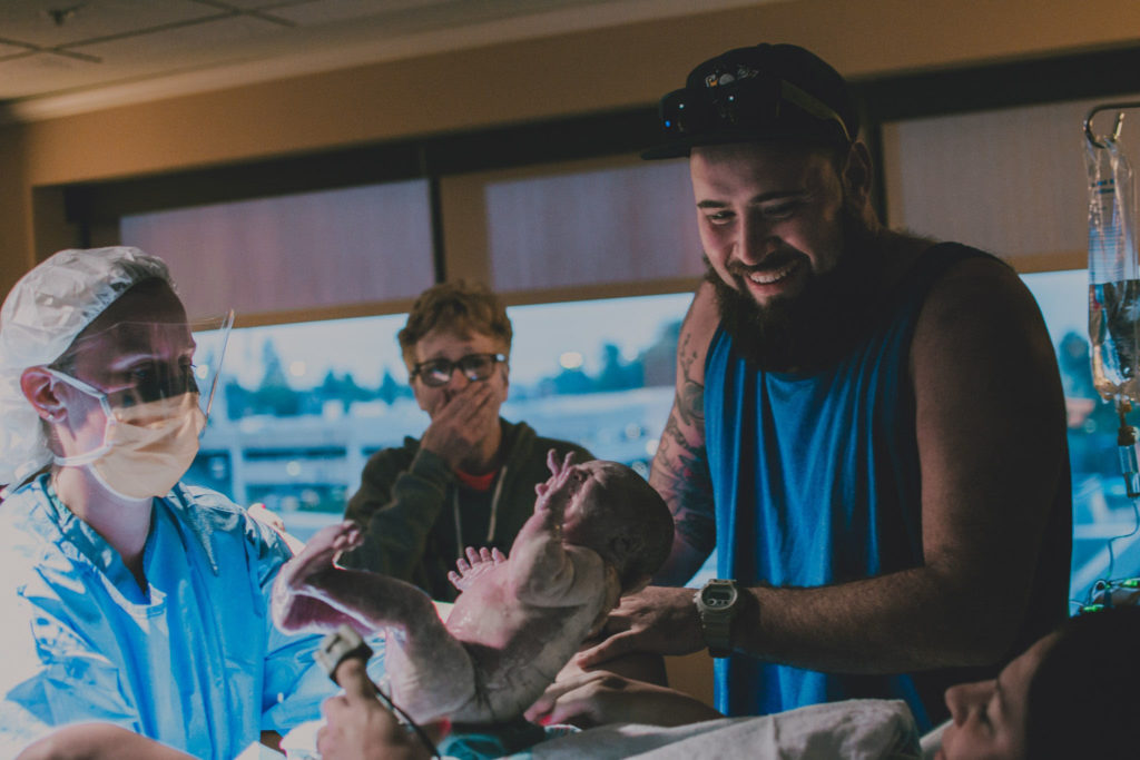 Dad smiles and baby girl is born, and grandma stands, astonished, in the background.