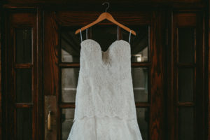 Beautiful white lace wedding dress hanging from a wooden door.