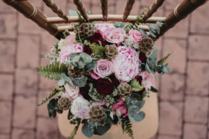 Stunning flower bouquet of deep red, pink, and soft shades of green, sitting atop a gold chair.