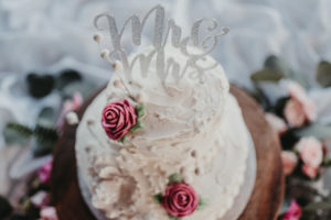 Top down shot of a gorgeous, roughly-iced cake with deep pink roses, and a sparkly "Mr & Mrs" topper.