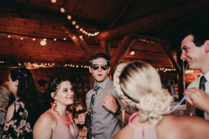A wedding guest wearing a glow stick as a headband, and sunglasses inside the reception venue.