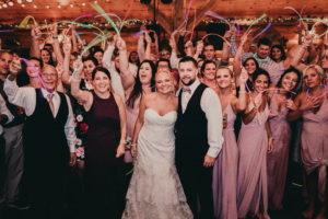 Bride and Groom stand among their guests while the guests wave glow sticks in the air.